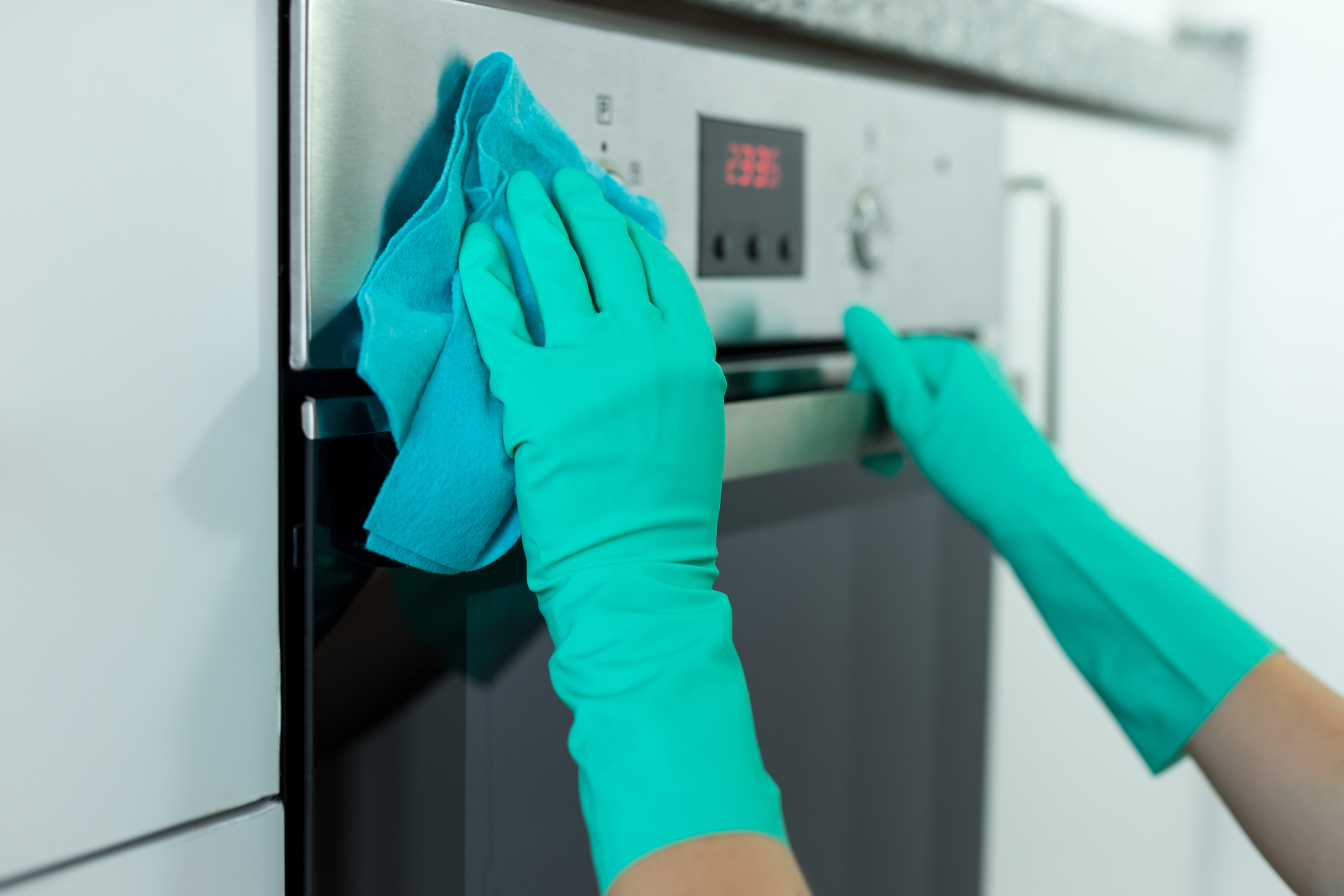 gloved hands cleaning oven exterior