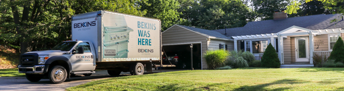 A Bekins delivery truck parked in front of a suburban home
