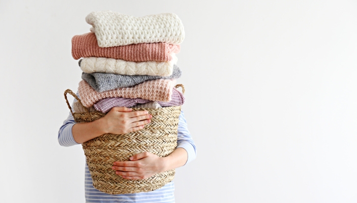 A person holds a very full basket of folded winter laundry.