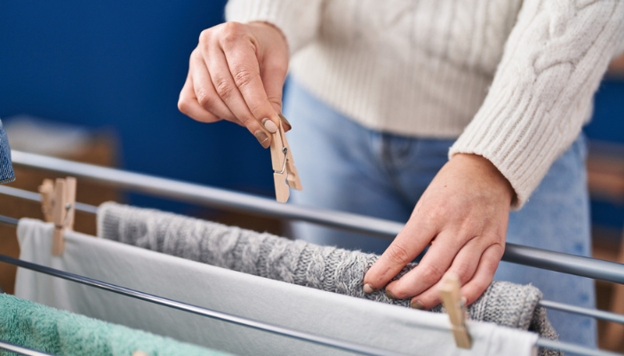 A pair of hands clips laundry onto a line indoors to air dry.