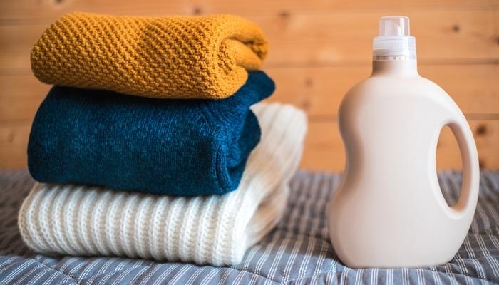 Folded sweaters next to bottle of detergent