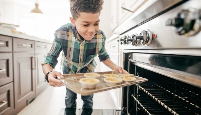 Young boy placing baked goods into oven