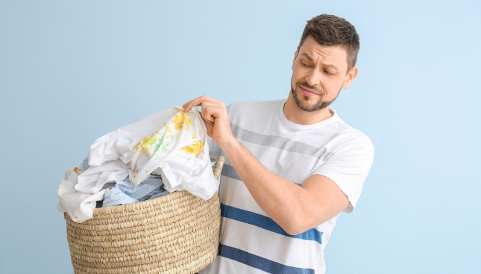 Man holding laundry basket with really dirty shirt on top