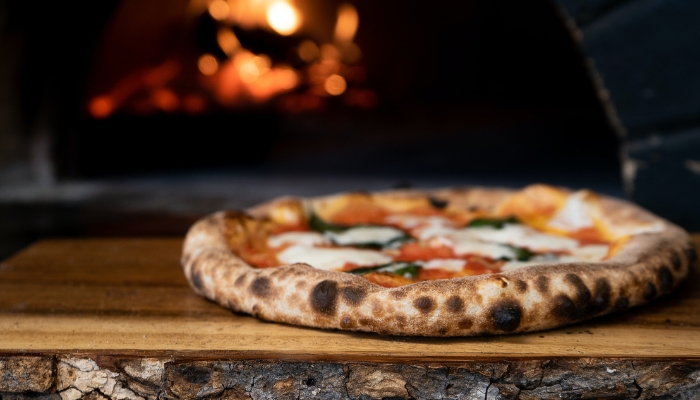 Crispy pizza in front of pizza oven on wood slab
