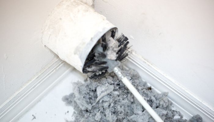 White and gray brush cleaning out a dryer vent with debris on the floor