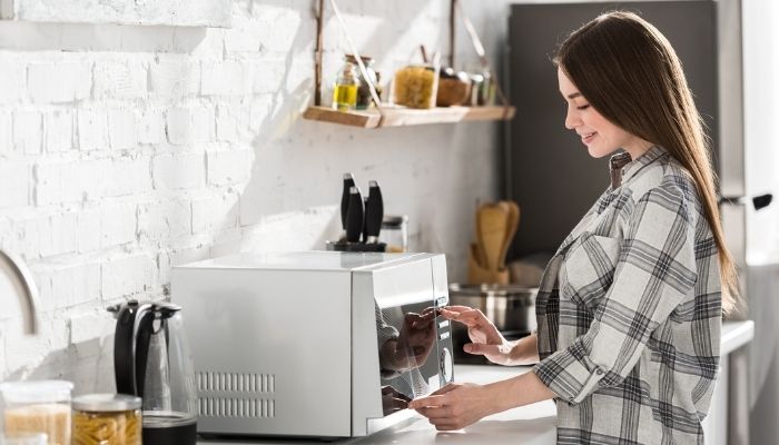 smiling woman using microwave oven in kitchen