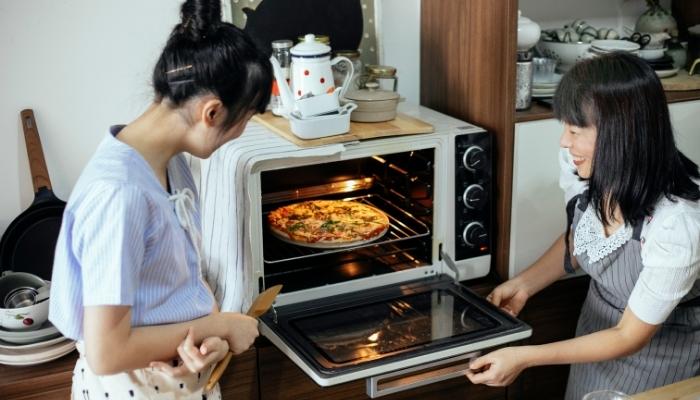 Two women making homemade pizza in small oven