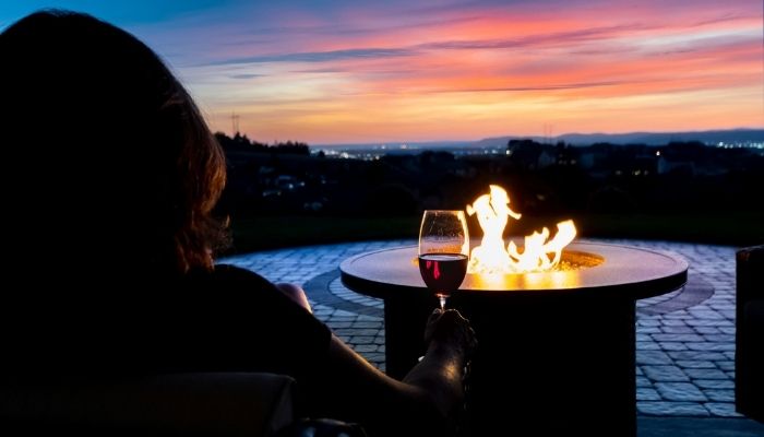 woman with a glass of red wine by a fire pit
