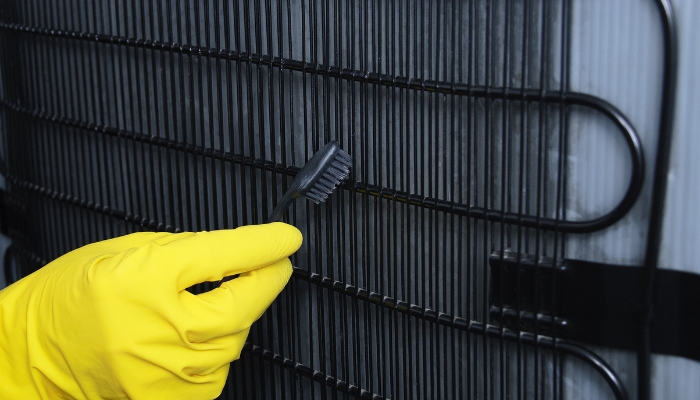Closeup of someone cleaning condenser coils on a fridge