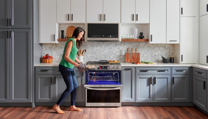 A woman opens the top section of a dual-oven to place food inside