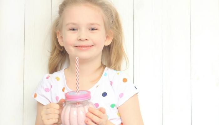 Little girl happily drinking berry smoothie