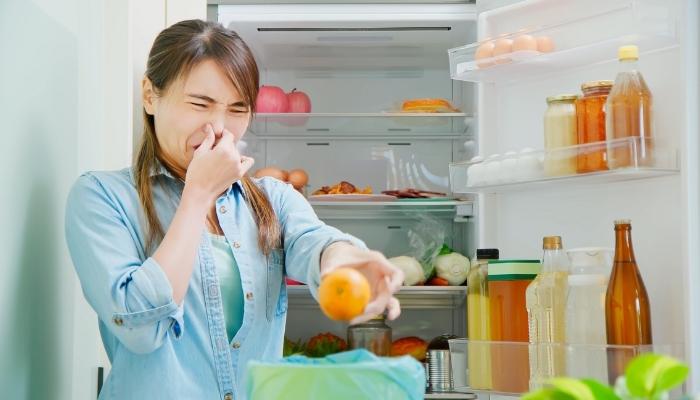 Woman pinching nose while removing spoiled food from fridge