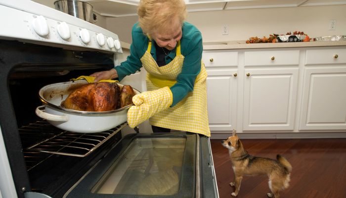 woman pulling roasted chicken out of oven 