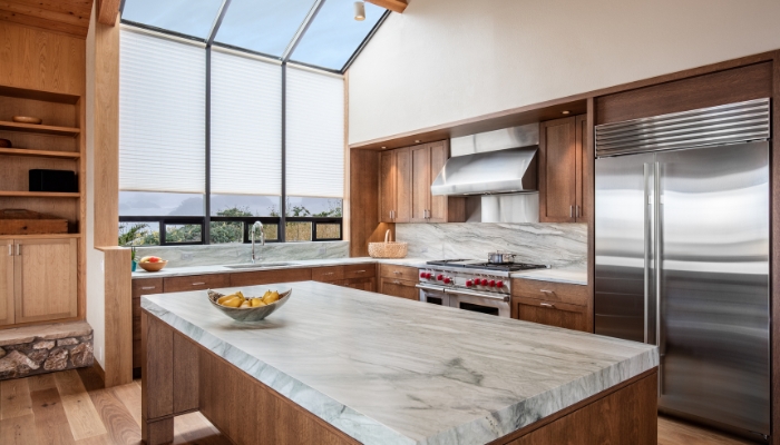 A kitchen with a lot of natural wood features, a large window, and stainless steel appliances.