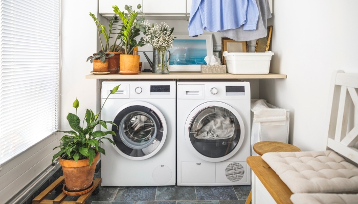A white washer and dryer is surrounded by plants in a laundry room.