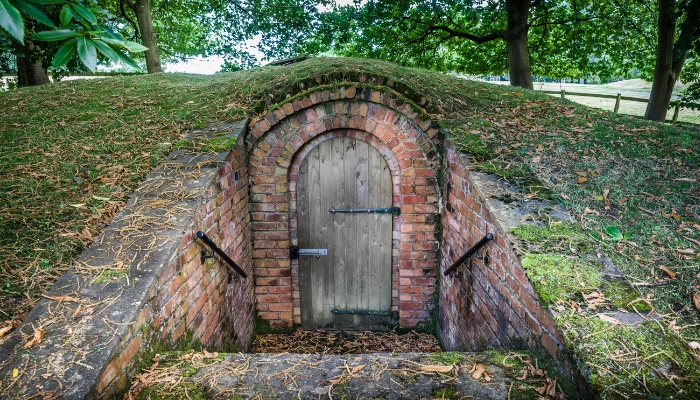An ice house sits in a grassy hill, the door is wooden and surrounded by red brink