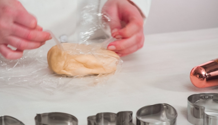 Hands unwrap a ball of sugar cookie dough from plastic wrap.
