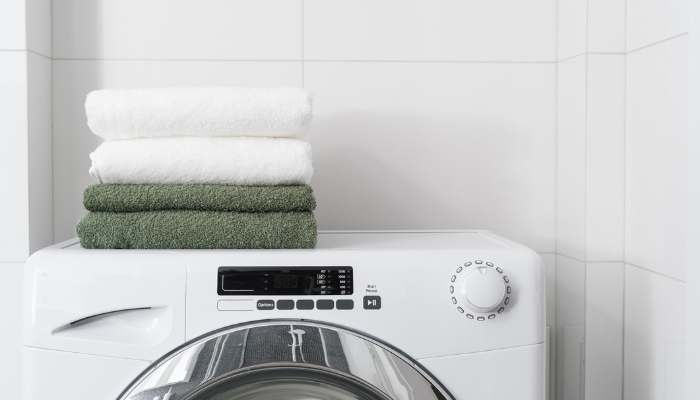 White and green towels are folded on top of a white washing machine.