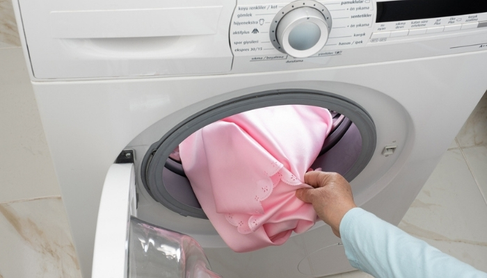 hand removing pink satin sheet from washer