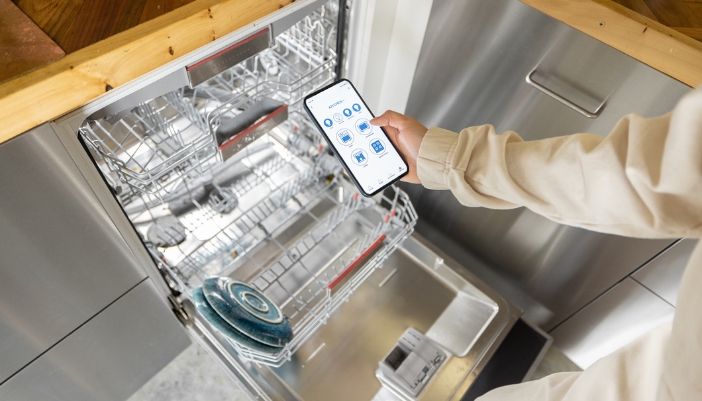 Closeup of someone holding up their smartphone next to their smart dishwasher