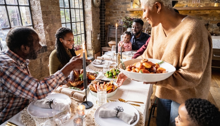 A family sits at a dining table and begins to eat their holiday meal.