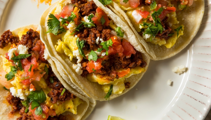Three breakfast tacos with meat and eggs are lying on a white plate.
