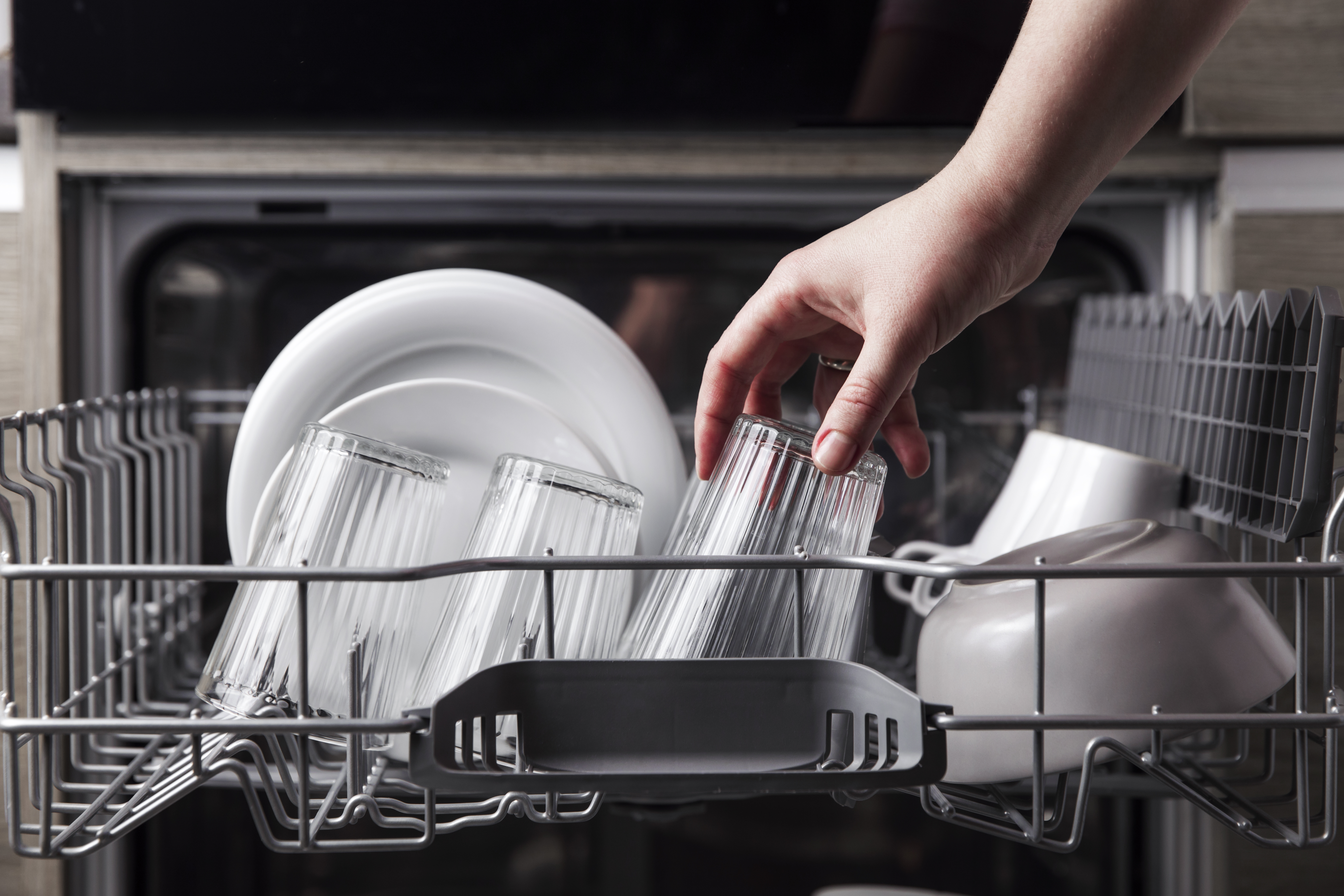 A person placing a glass on the upper rack of a dishwasher 