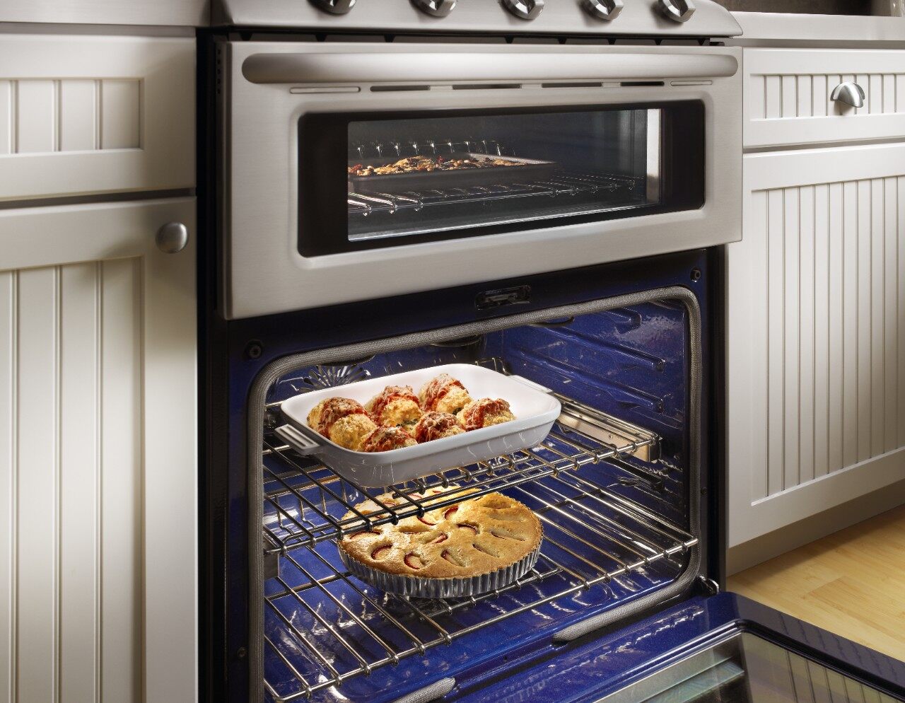 A pie and an entrée baking inside of a KitchenAid double oven gas range