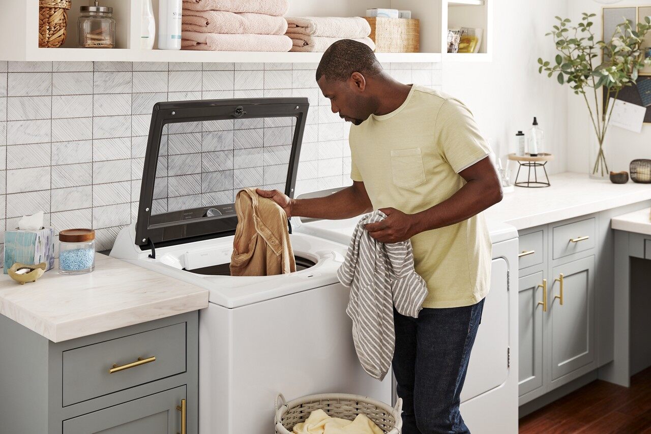 A man in a yellow shirt grabbing items out of a Whirlpool top load washer 