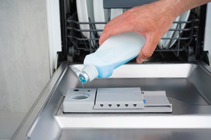Hand filling dishwasher with liquid into the dishwasher box.