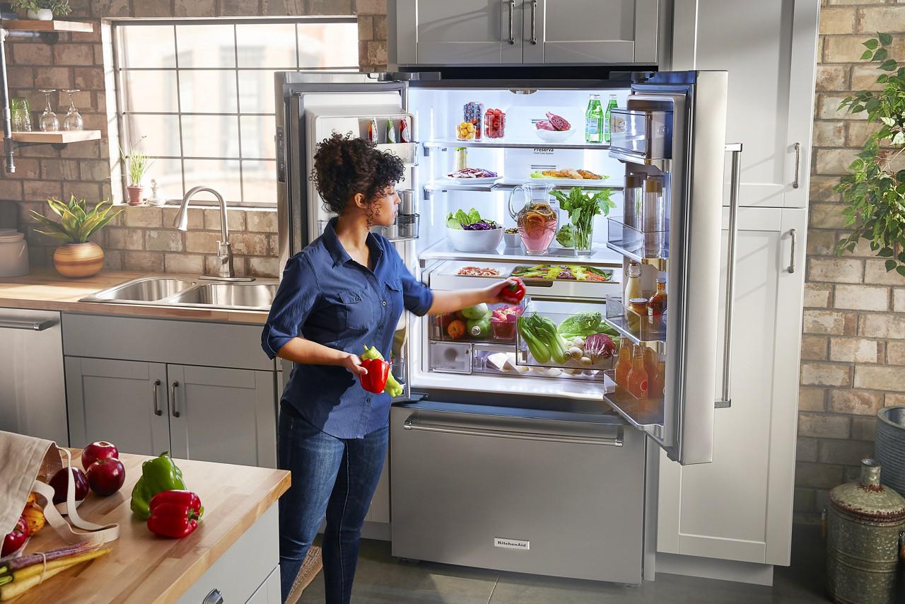 woman retrieves bell peppers from KitchenAid French door refrigerator
