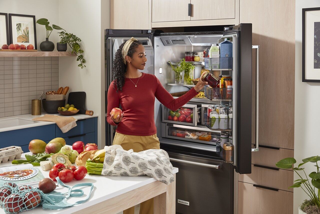 Women grabbing items from an open KitchenAid black stainless steel refrigerator 