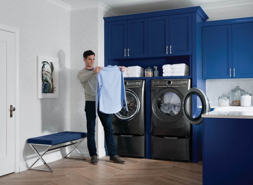 man doing his laundry and holding up his dress shirt 