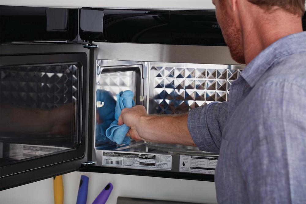 man wipes down walls of his over-the-range microwave