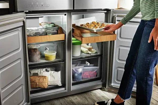A woman placing a tray of cookie dough into the KitchenAid KRQC506MPS 4-door refrigerator 
