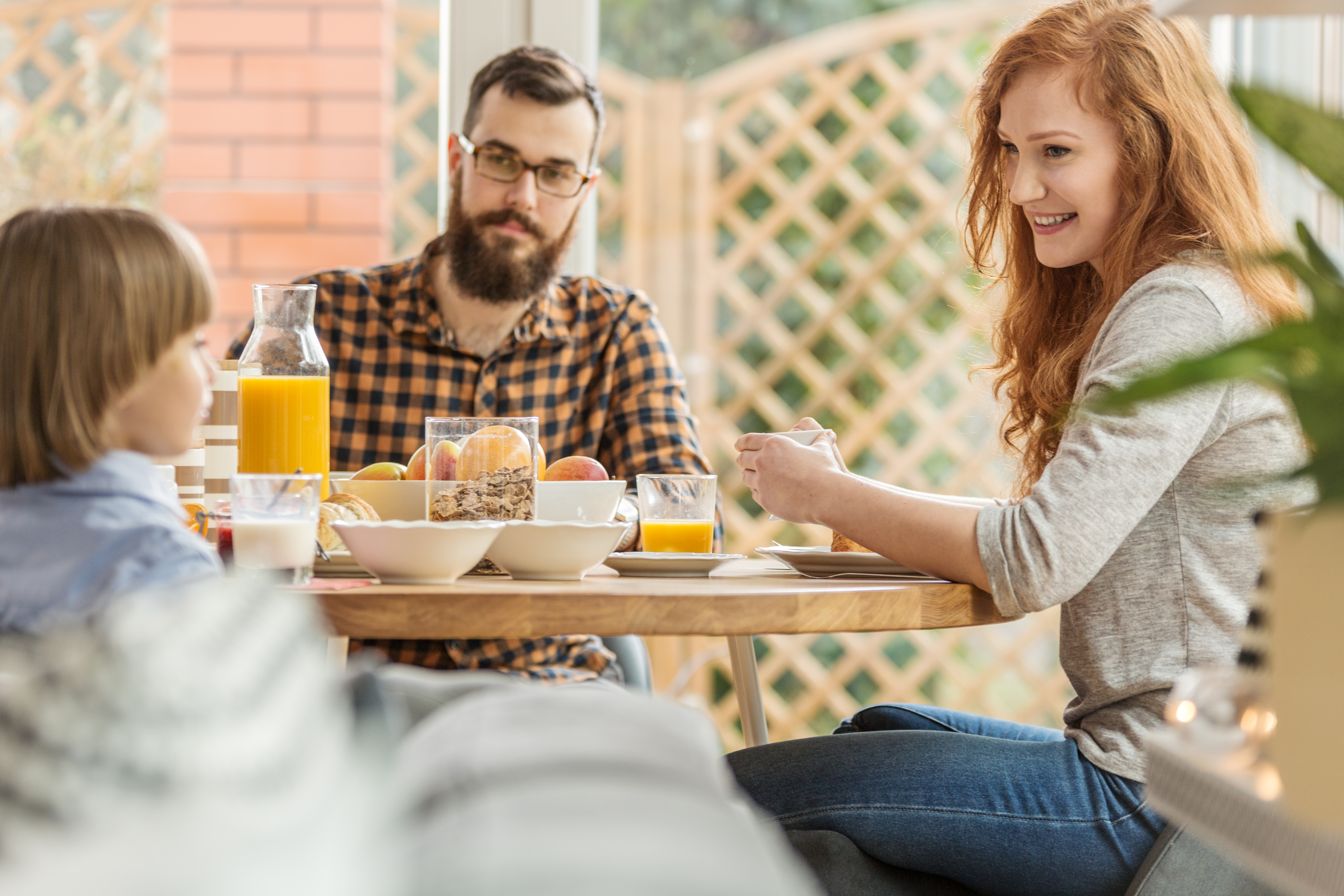 Man, woman, and child enjoy eating breakfast outdoors on a patio 