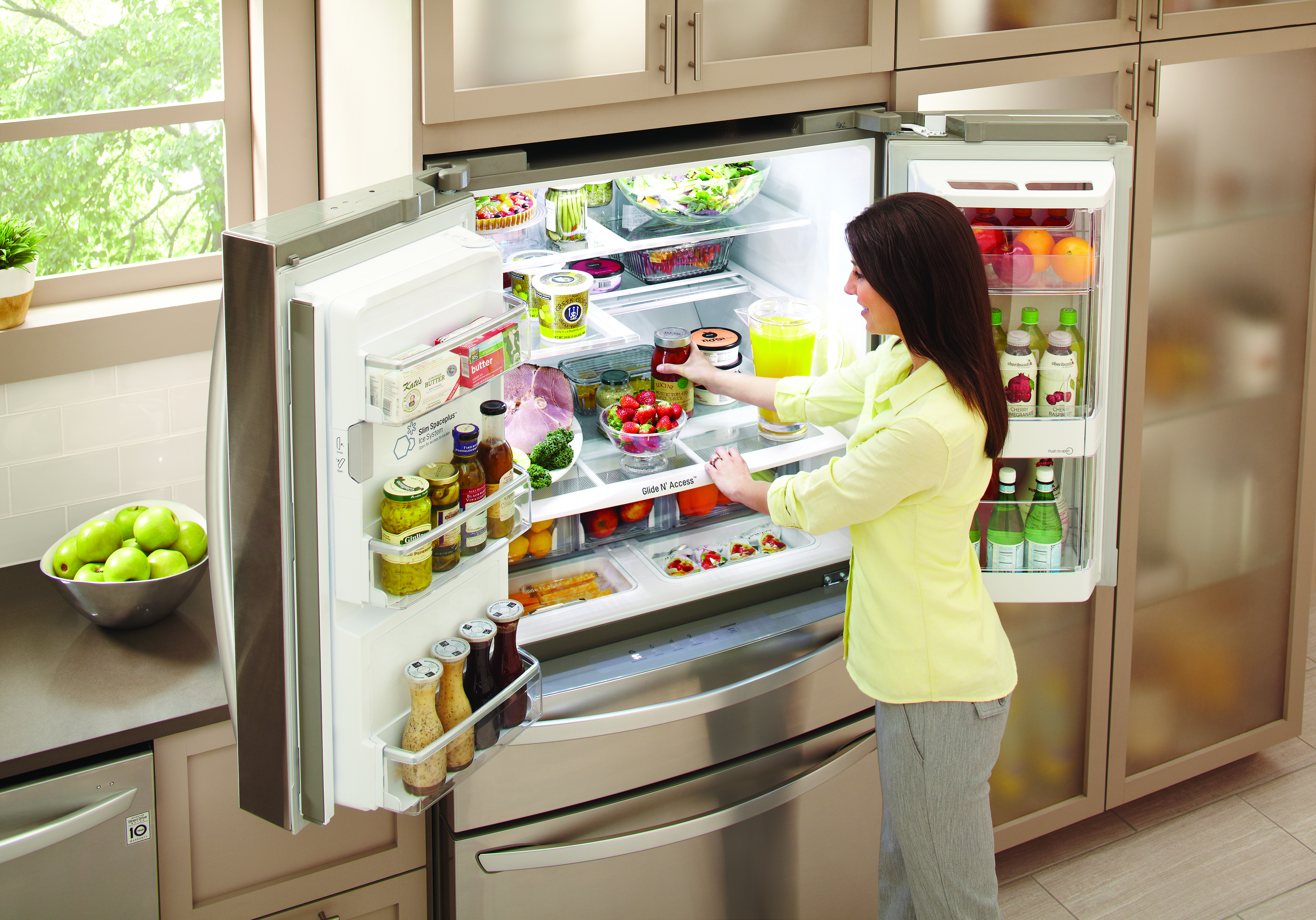 woman in yellow button up shirt stocks items into french door fridge with both doors open