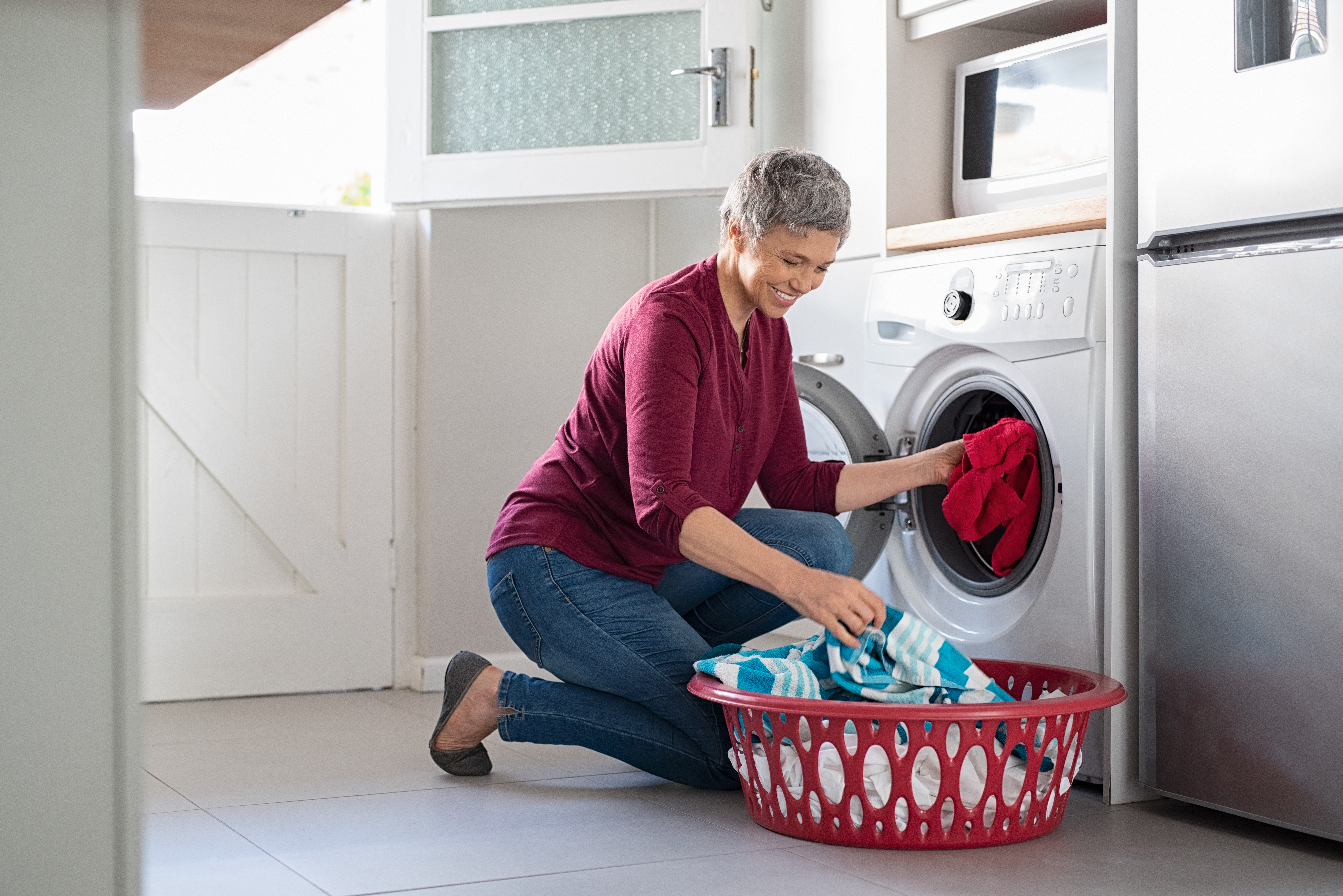 woman in burgundy shirt and jeans taking clothes our of front load washer