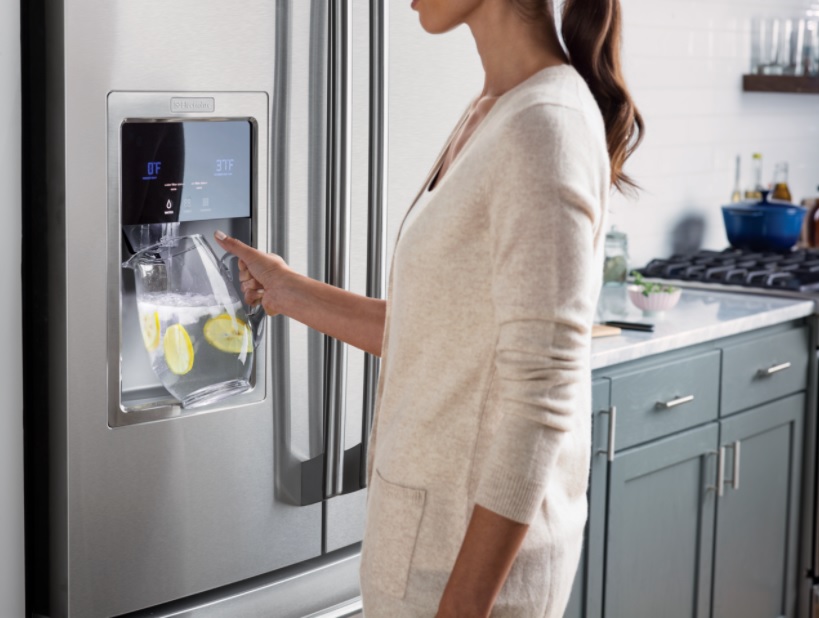 woman uses water dispenser on an Electrolux refrigerator to pour water in pitcher