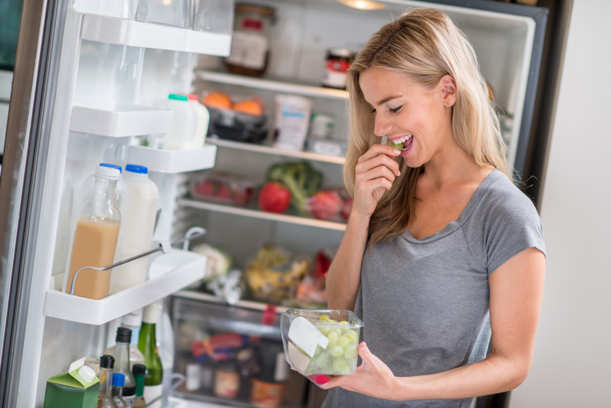 young woman eats grapes she retrieved from her bottom freezer refrigerator