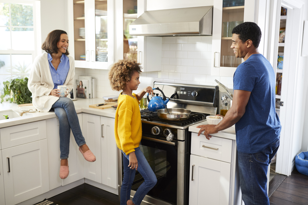 young girl cooks breakfast on gas range while parents look on