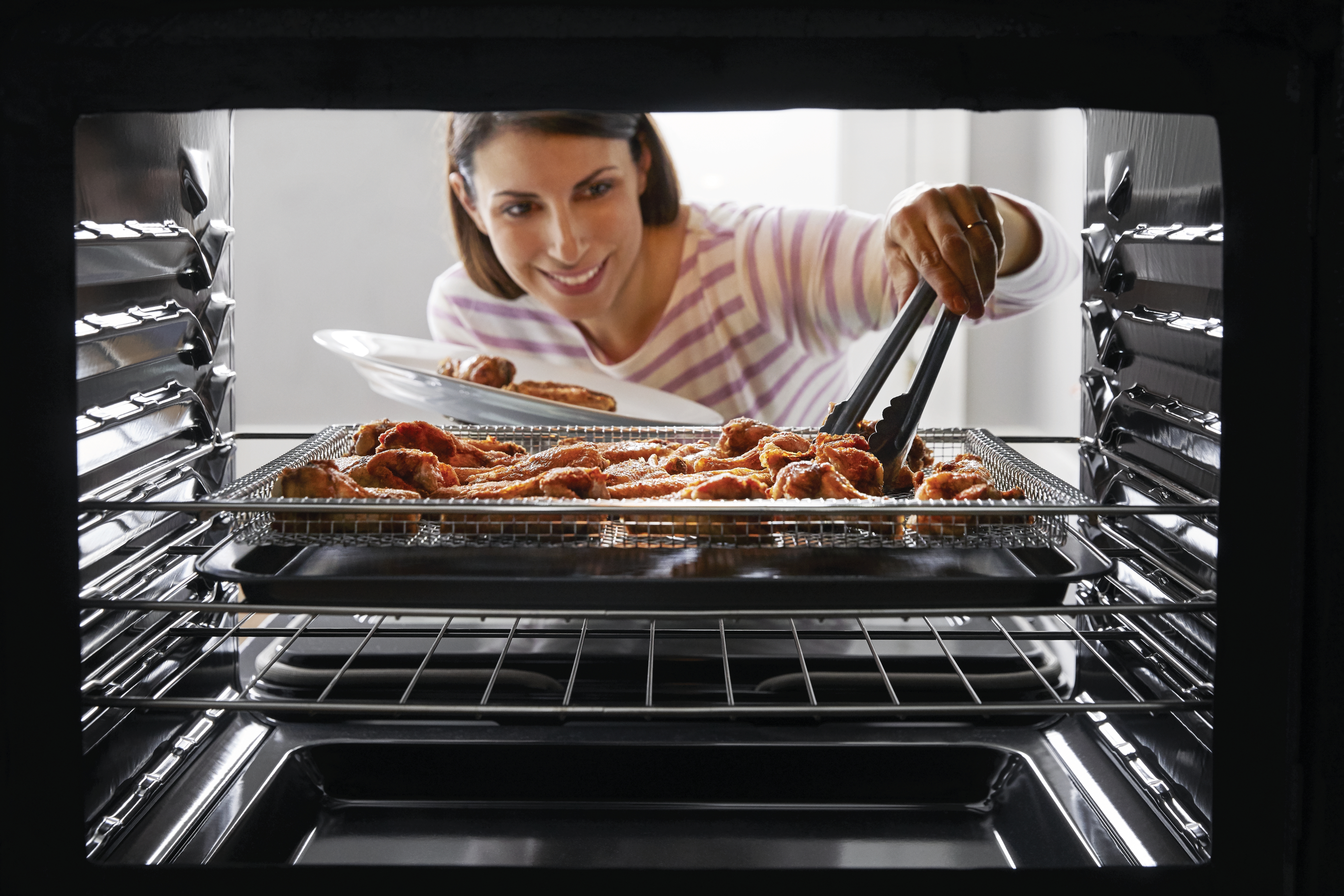 Woman retrieving a tray of chicken wings from inside a Frigidaire Gallery Air Fry oven 