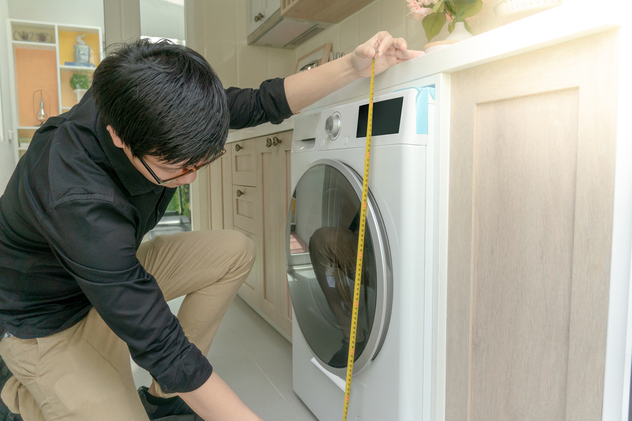 Man in black shirt and khakis measures the height of a front-loading washing machine