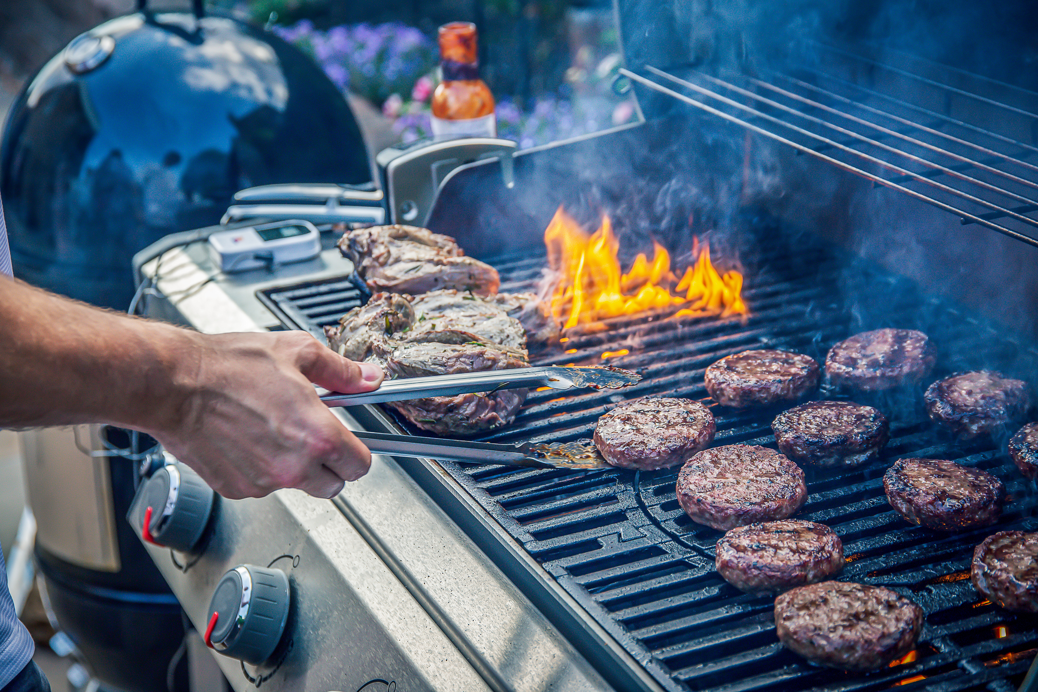 man flipping burgers and steaks on a gas grill