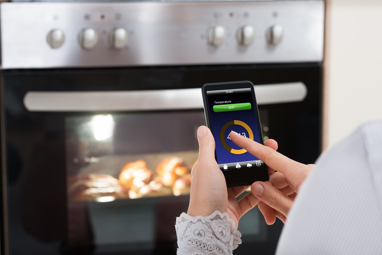 closeup of a woman operating wall oven with smartphone
