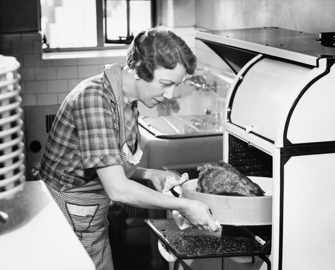 black-and-white photograph of housewife removing turkey from retro oven