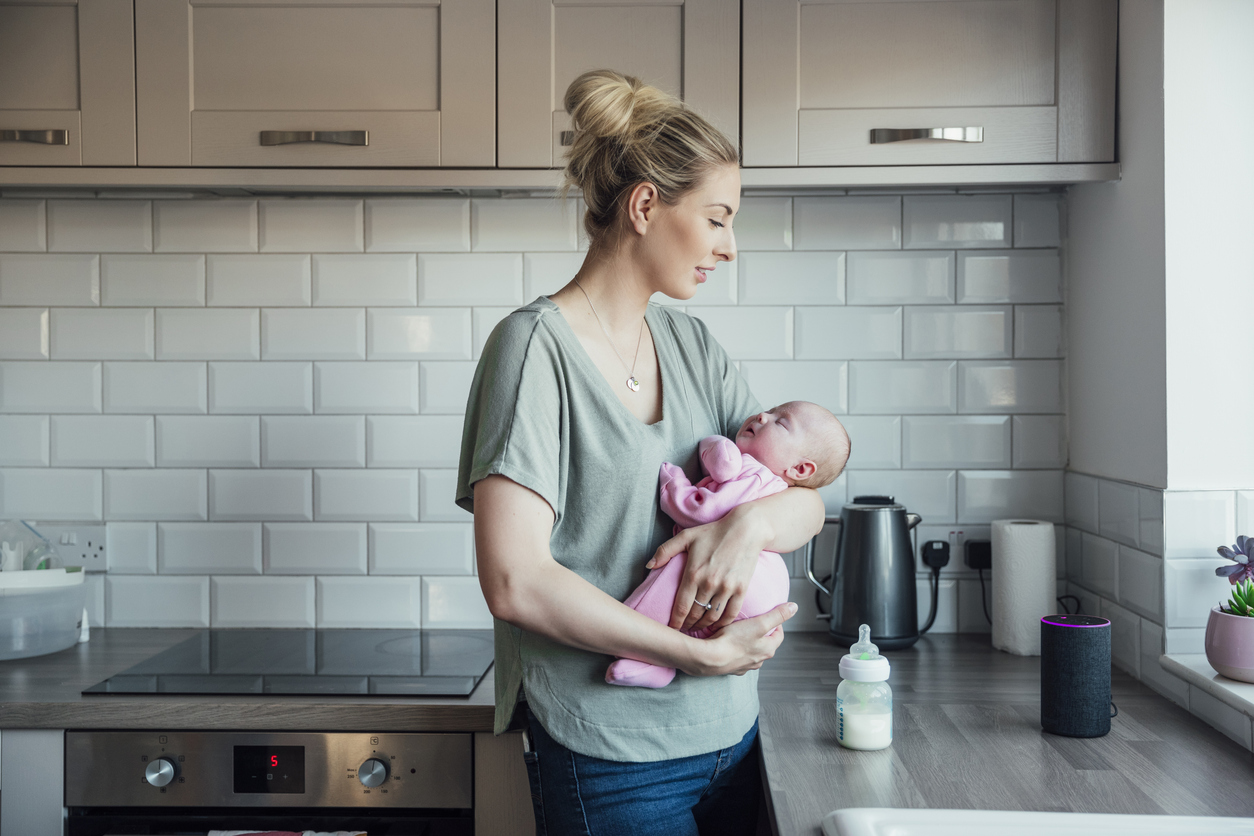 young woman standing in her kitchen holding her newborn daughter in her arms