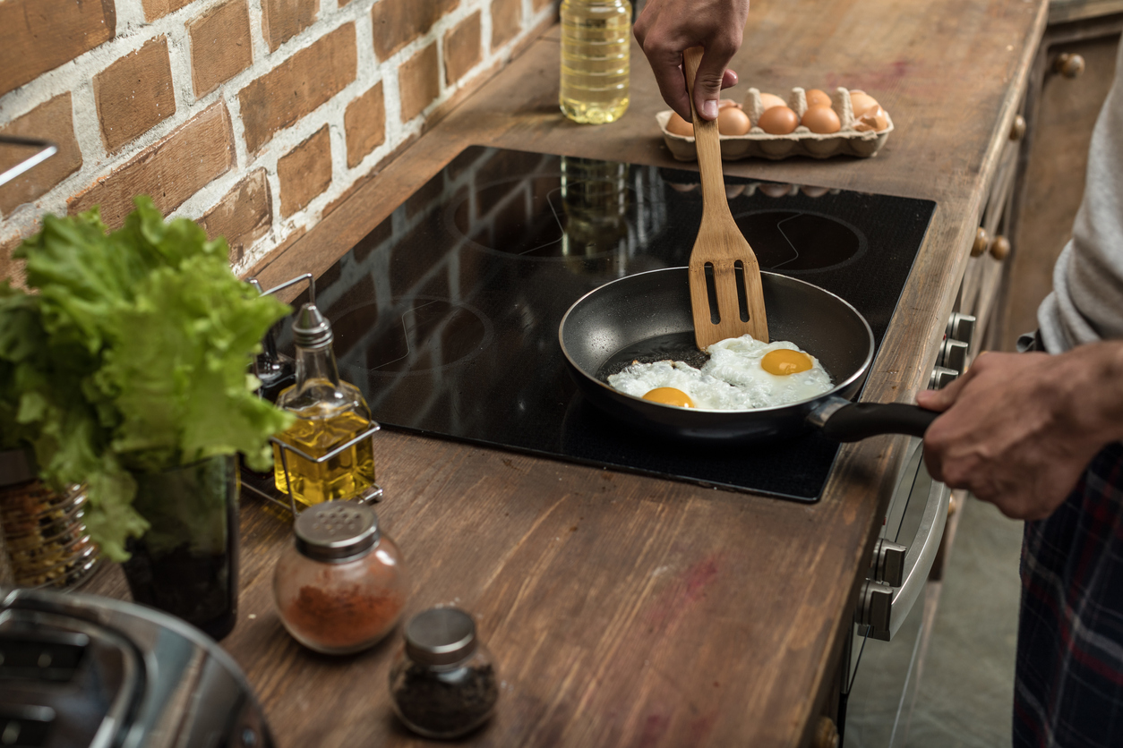 young man prepares eggs on induction cooktop at home