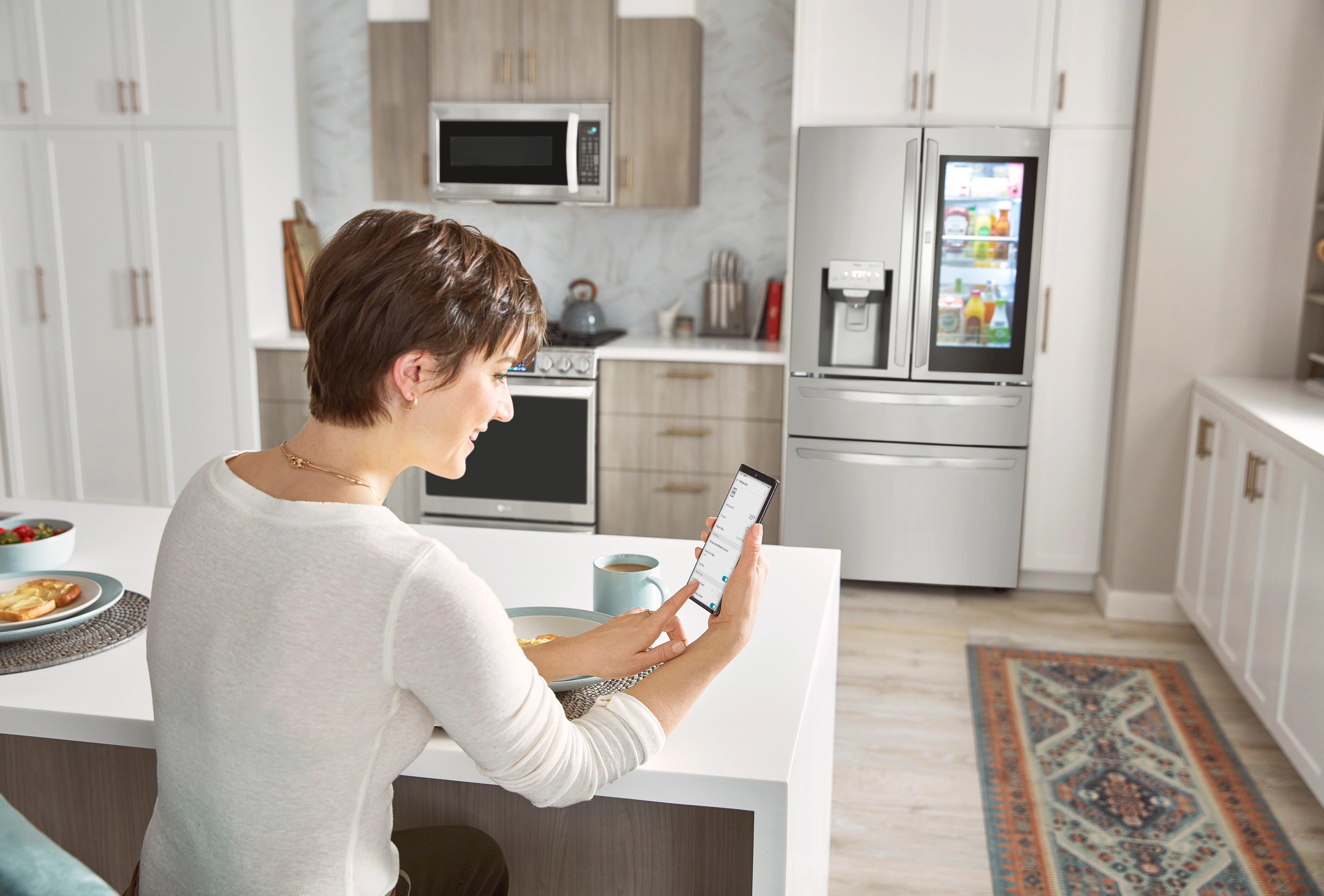 young woman uses ThinQ app to monitor her LG InstaView refrigerator
