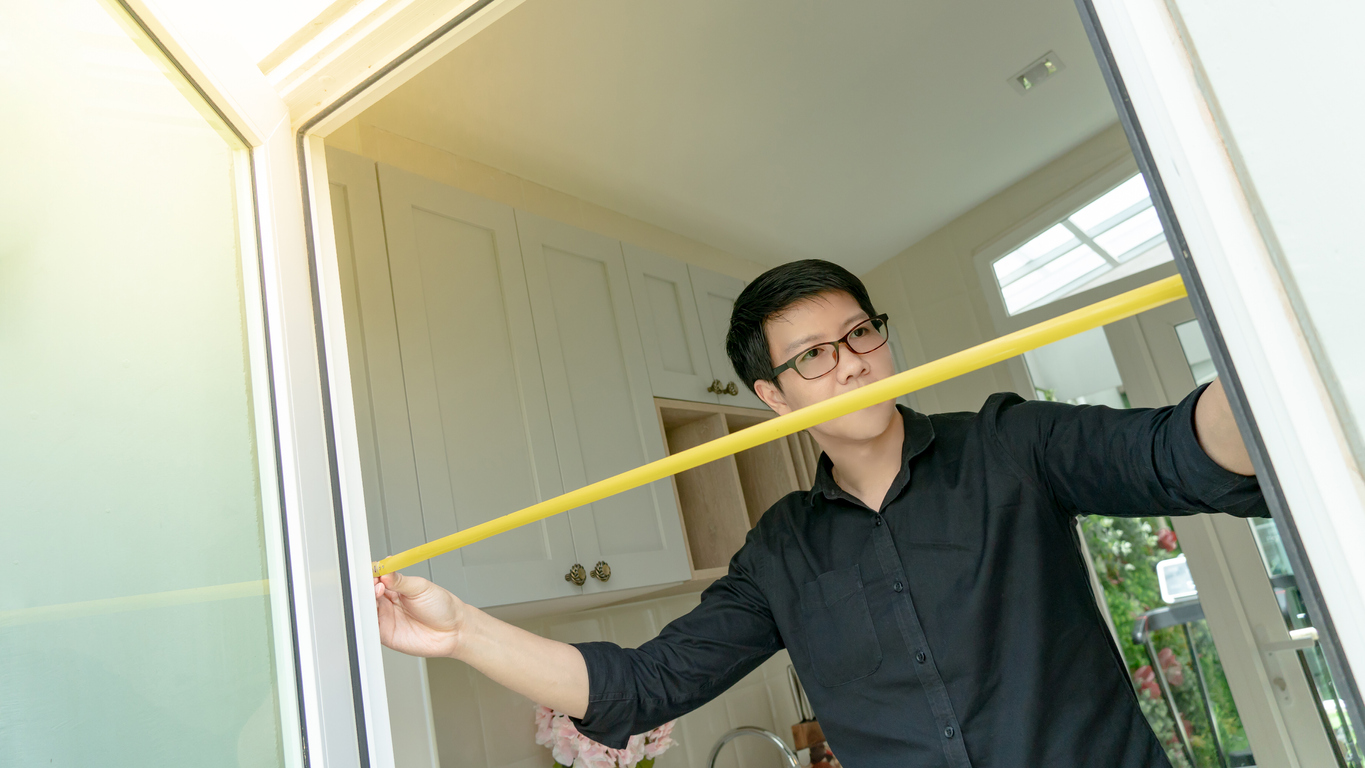 young man uses tape measure to check width of kitchen doorway